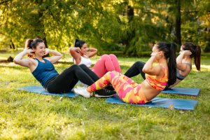 Four beautiful motivated female friends doing stomach exercises in the city park.